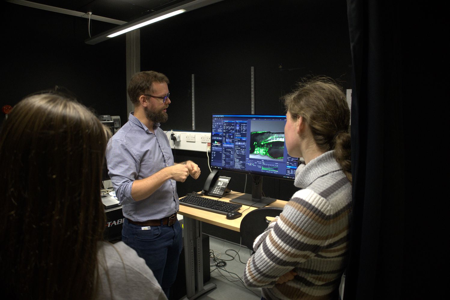 IDRM scientist talking and demonstrating laboratory imaging equipment to a small group of students