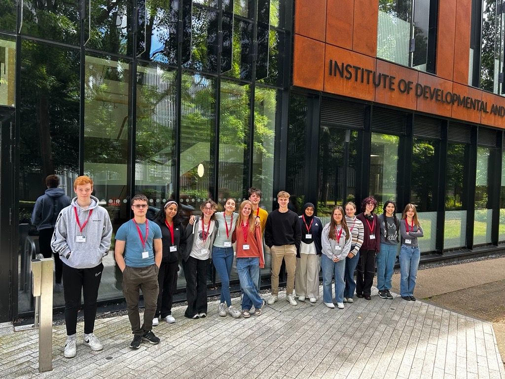 Fourteen sixth-form students are standing side-by-side in a line outside the front door of the Institute of Developmental & Regenerative Medicine